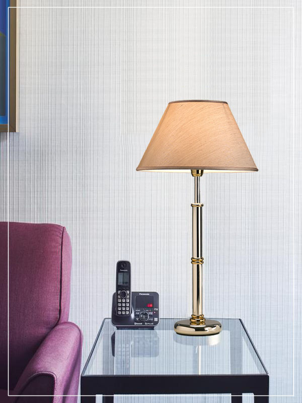 Επιτραπέζιο φωτιστικό με επιμεταλλωμένη βάση σε χρυσό χρώμα σε δωμάτιο ξενοδοχείου.